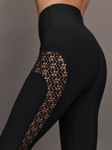 Model wears a pair of black high waisted leggings with laser cutouts along thighs. 