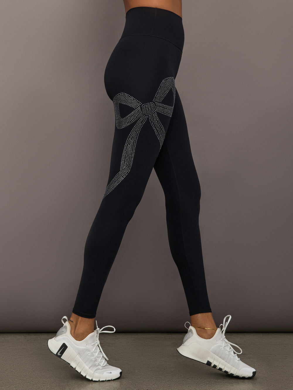 Model wearing Rhinestone Bow Legging in Melt Black, side view highlighting rhinestone bow detail.