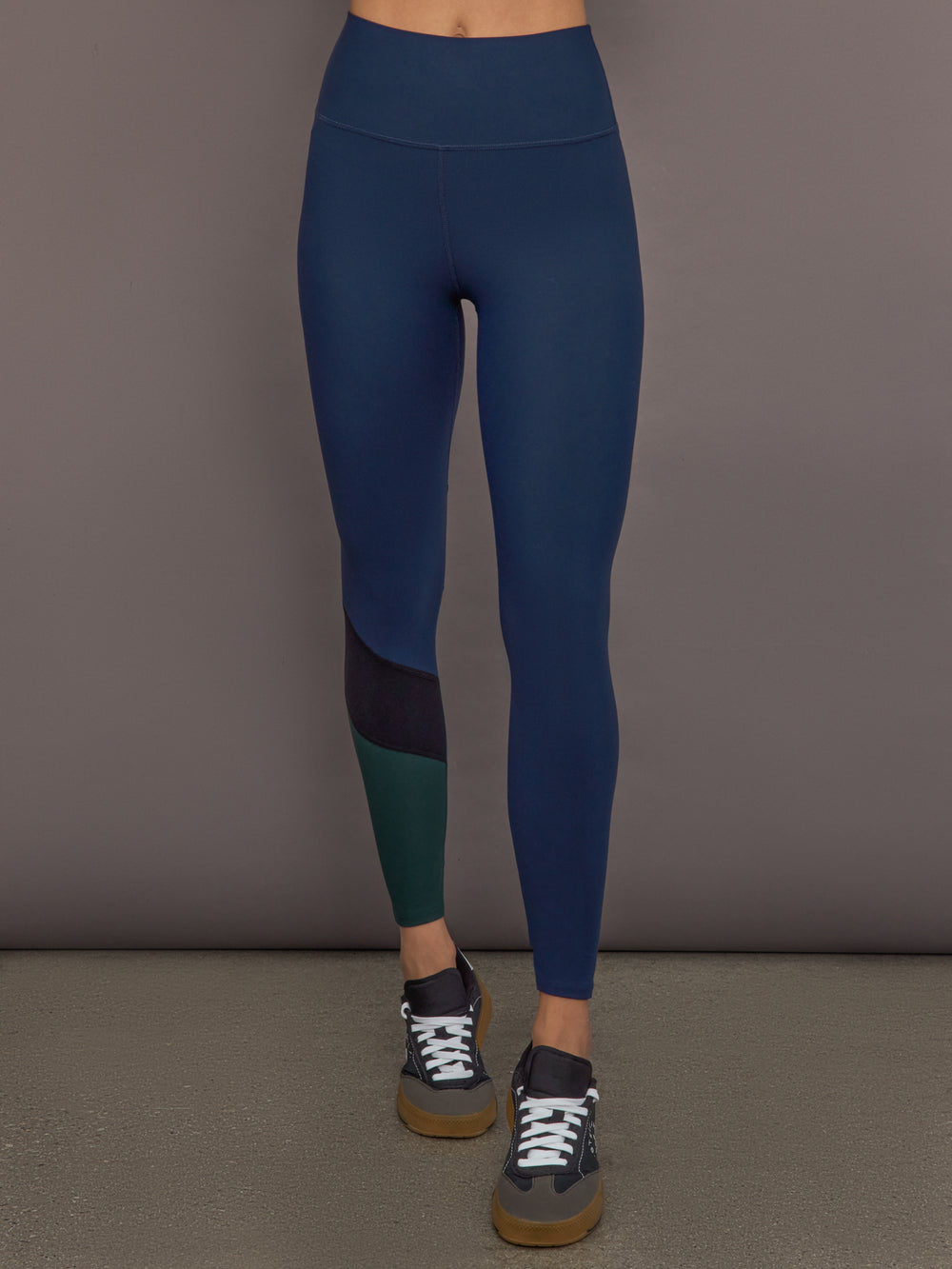 Model is wearing Melt High-Waisted Colorblock Legging in Navy, Black, and Forest, front view.