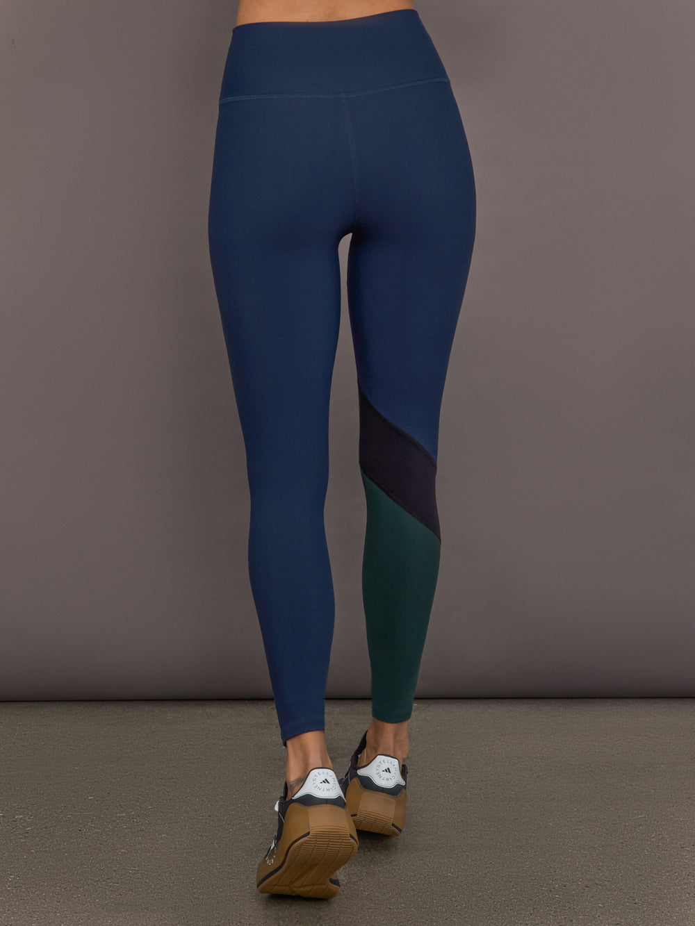 Model is wearing Melt High-Waisted Colorblock Legging in Navy, Black, and Forest, back view.