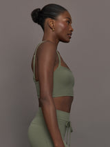 Model wears a buttery soft sports bra in army green with double straps and cross back design. 