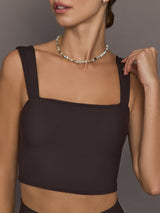 Model is wearing a dark brown square-neck cropped tank top with wide straps and a fitted silhouette, close-up front view.