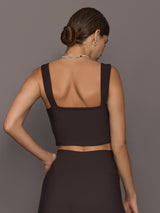 Model is wearing a dark brown square-neck cropped tank top with wide straps and straight back design, styled with matching high-rise leggings, back view.
