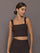 Model is wearing a dark brown square-neck cropped tank top with wide straps and a fitted silhouette, front view.