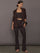 Model is wearing a dark brown square-neck cropped tank top styled with matching high-rise flared leggings, layered with a tailored blazer, brown flats, pearl necklace, and woven clutch, front view.