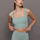 Model wears sage green bra top with a square neckline and wide shoulder straps.