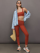 Model is wearing ribbed terracotta high-rise leggings styled with matching bra and denim jacket, full body view.