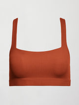 Model wears terracotta-colored racerback bra with a ribbed texture, square neckline, and wide straps that merge at the back.
