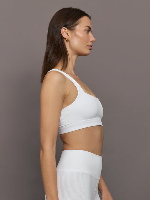 Model wears ribbed, white racerback sports bra with a fitted design and square neckline.
