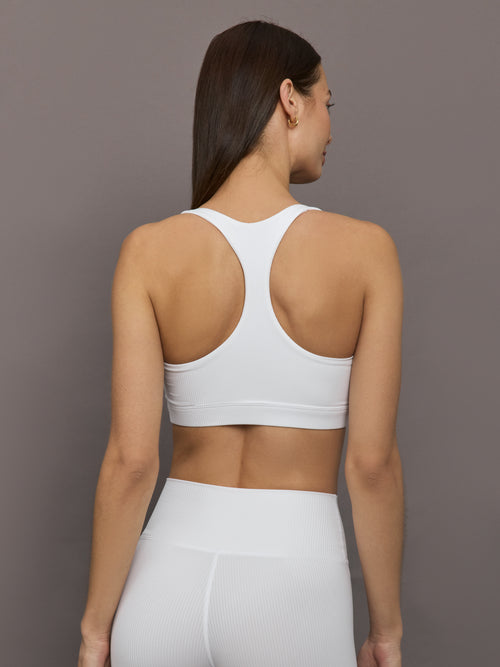 Model wears ribbed, white racerback sports bra with a fitted design and square neckline.
