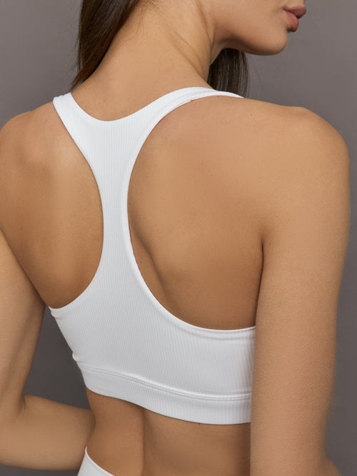 Model wears ribbed, white racerback sports bra with a fitted design and square neckline.

