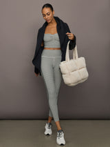 Full outfit view of houndstooth sports bra with matching leggings, styled with black jacket, white tote, and sneakers.