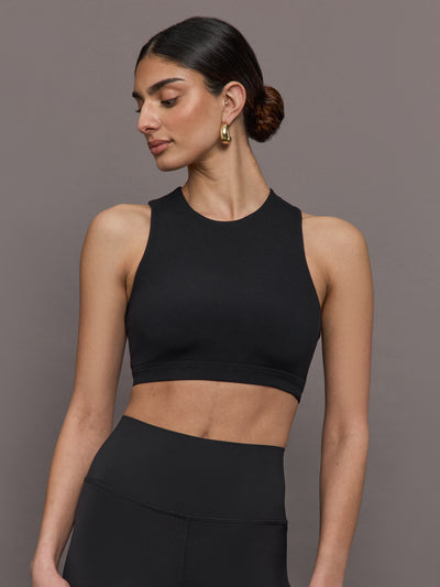 Model wears a cropped black athleisure tank with an asymmetrical racerback. 