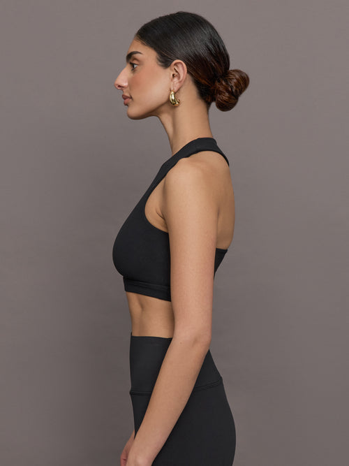 Model wears a cropped black athleisure tank with an asymmetrical racerback. 