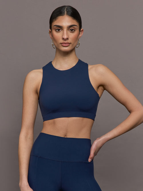 Model wears a cropped navy athleisure tank with an asymmetrical racerback. 