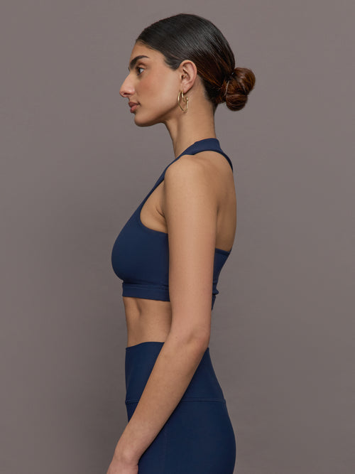 Model wears a cropped navy athleisure tank with an asymmetrical racerback. 