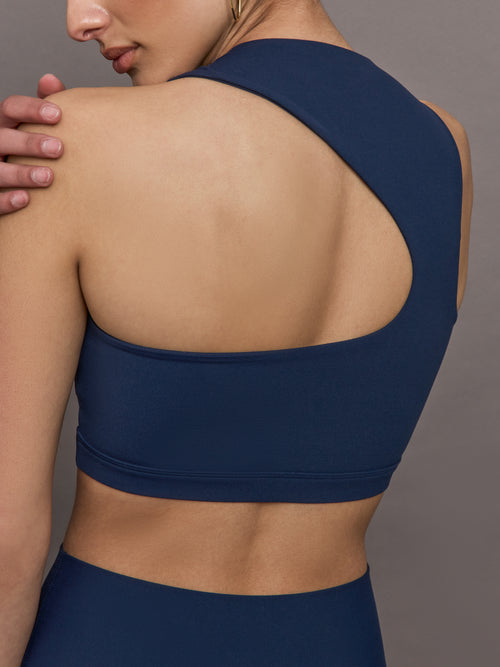 Model wears a cropped navy athleisure tank with an asymmetrical racerback. 