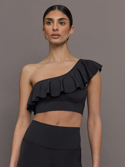 Model wears a black one shoulder sports bra with a ruffled overlay. 