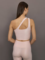 Model wears shiny, asymmetrical one-shoulder bra top in light pink, with a smooth, reflective fabric.