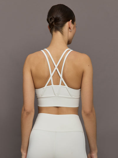 Model wears white active bra with double thin back straps and a smooth, supportive finish.

