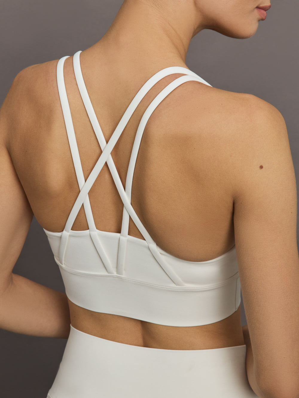 Model wears white active bra with double thin back straps and a smooth, supportive finish.
