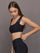 Model wears Black sports bra with double straps on one side and a square neck.