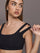 Model wears Black sports bra with double straps on one side and a square neck.