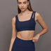 Model wears Navy sports bra with double straps on one side and a square neck.