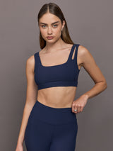 Model wears Navy sports bra with double straps on one side and a square neck.