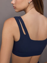 Model wears Black sports bra with double straps on one side and a square neck.