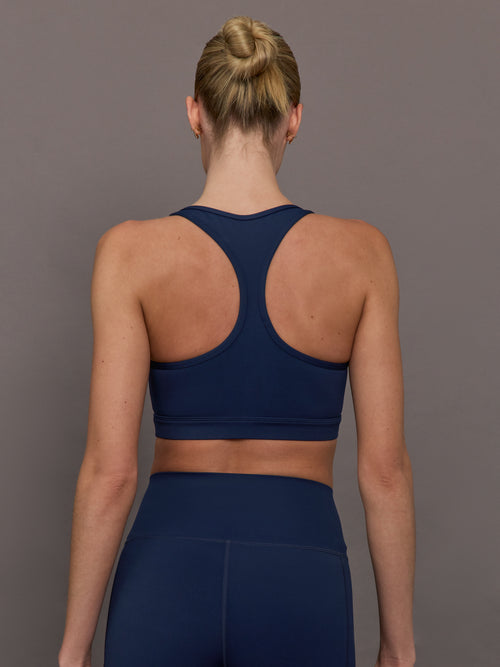 Model wearing a navy blue sports bra with zipper in the middle.