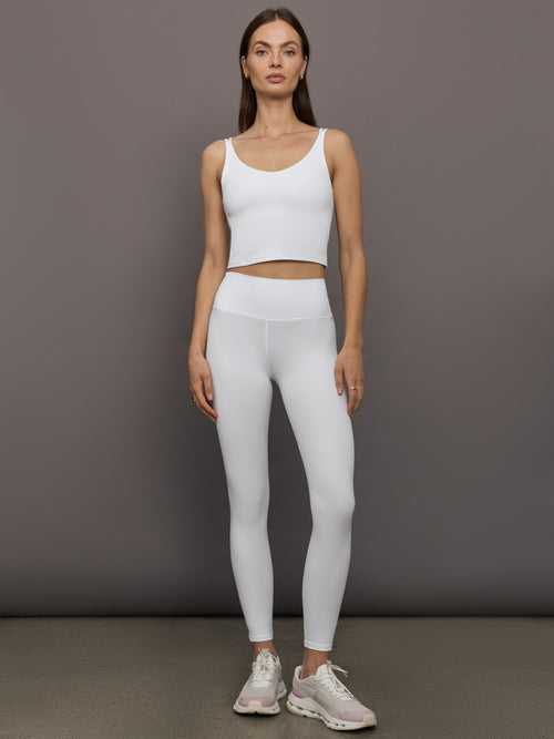 Model wears white ribbed V-neck tank with a sculpted and cropped fit.
