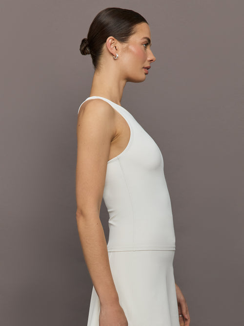 Model wears white high-neck active tank with a racerback design and smooth, fitted finish.
