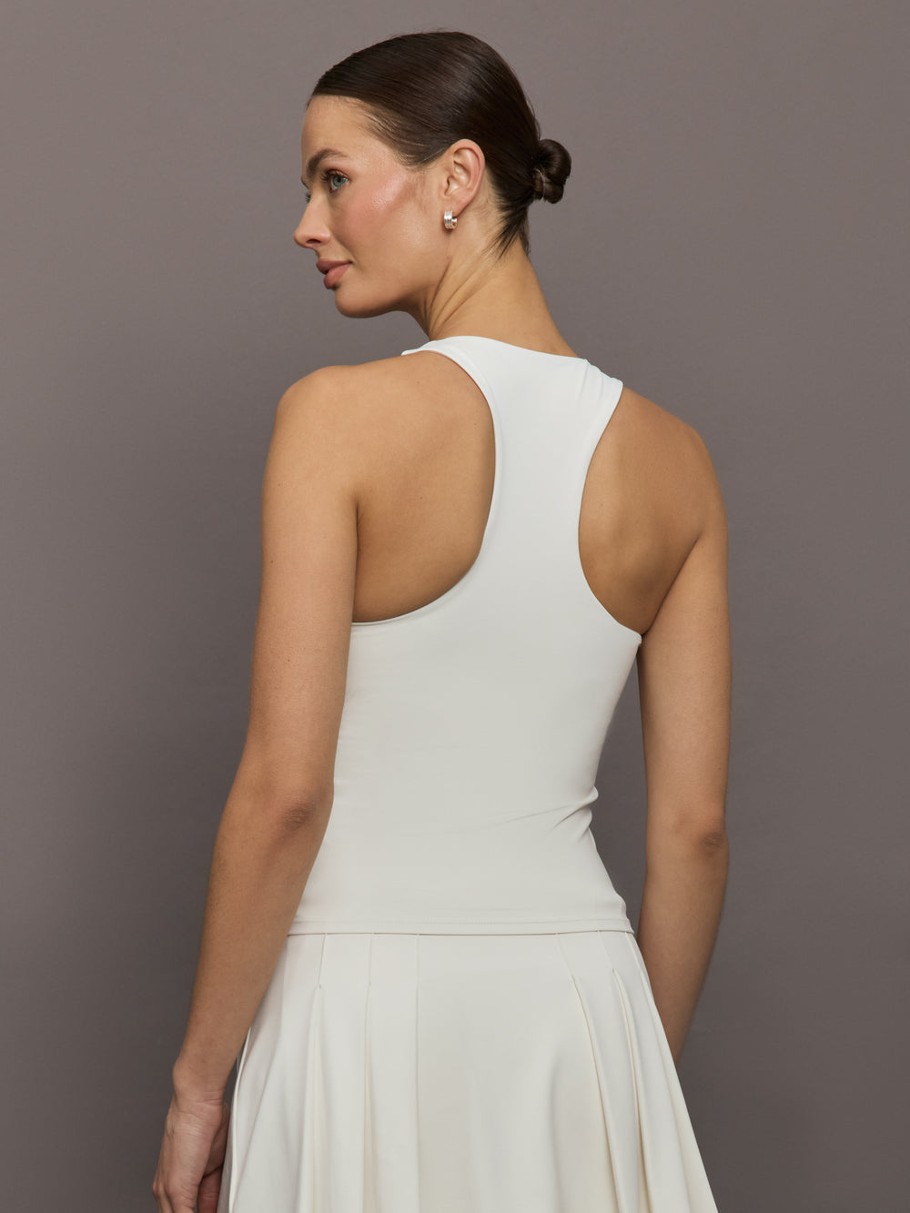 Model wears white high-neck active tank with a racerback design and smooth, fitted finish.
