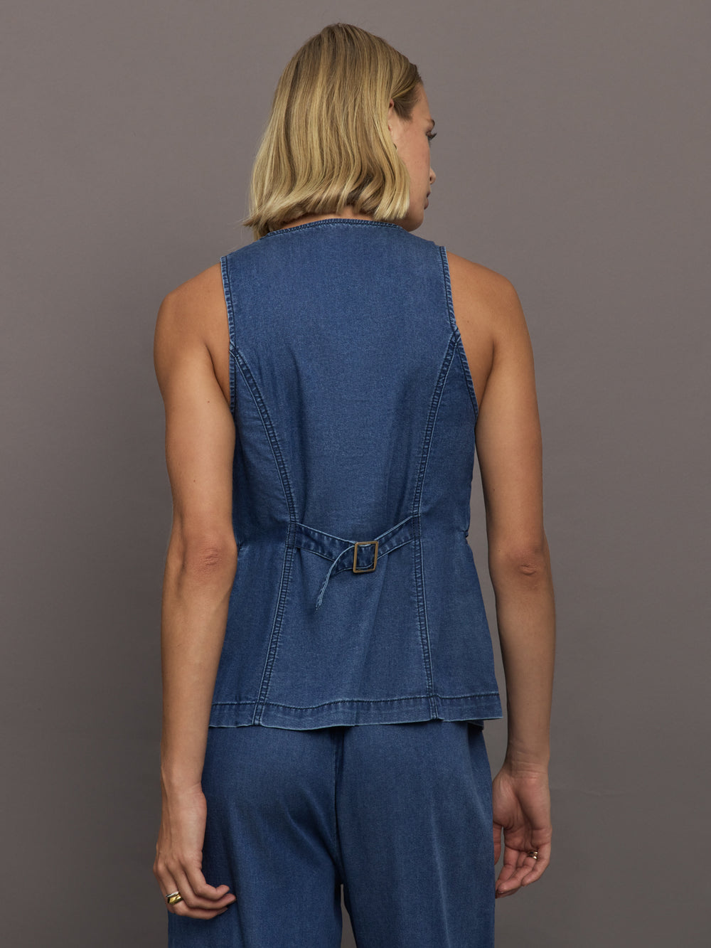 Model wears medium wash vest with a button-down front and sleeveless design.