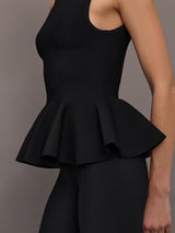 Woman wearing a sleeveless black peplum top against a gray background.