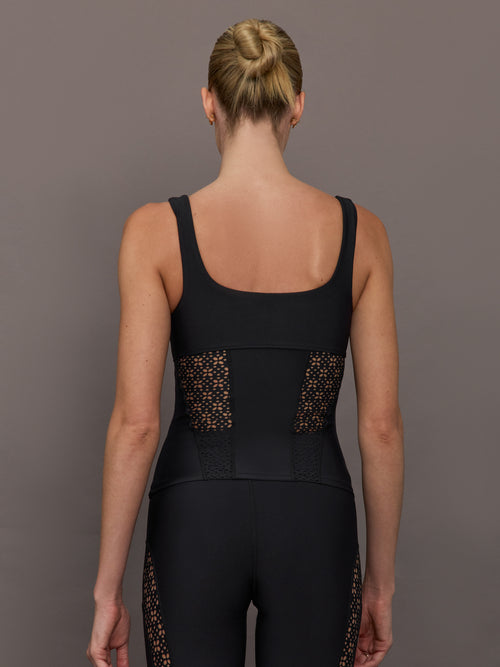 Model wears a black tank top with laser cutout paneling along riblines bilaterally. 