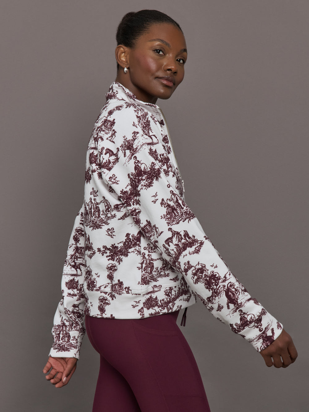 Model wears a burgundy toile printed mock neck zip up long sleeve track sweatshirt.
