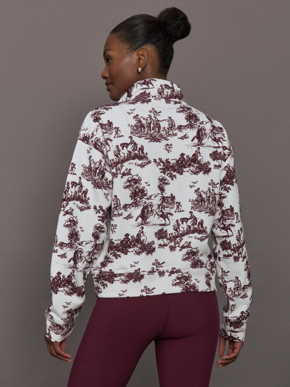 Model wears a burgundy toile printed mock neck zip up long sleeve track sweatshirt.