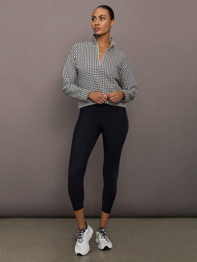 Full body view of houndstooth half-zip pullover styled with black leggings and sneakers.