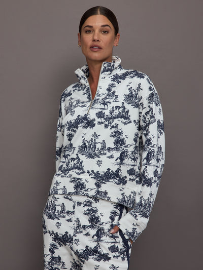 Woman wearing a white track jacket with blue floral toile pattern against a gray background.