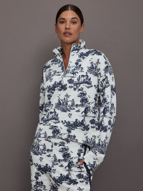 Woman wearing a white track jacket with blue floral toile pattern against a gray background.