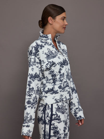 Woman wearing a white track jacket with blue floral toile pattern against a gray background.