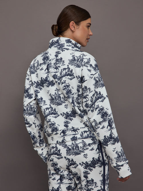 Woman wearing a white track jacket with blue floral toile pattern against a gray background.
