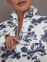 Woman wearing a white track jacket with blue floral toile pattern against a gray background.