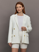 Model wears the white double-breasted blazer in Scuba, with a tailored fit, and a smooth, contoured finish.