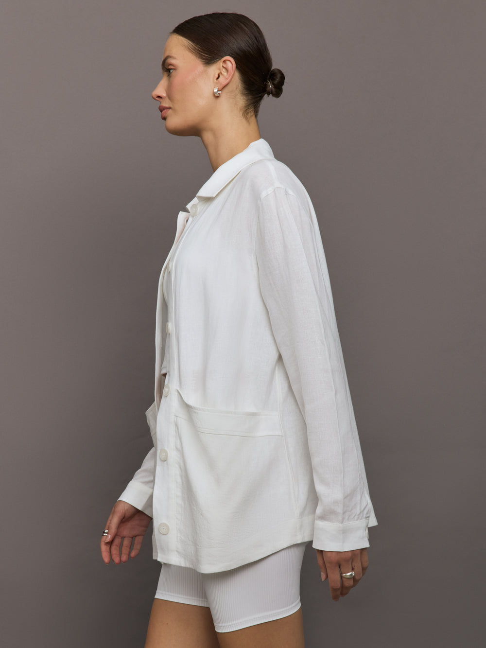 Model wears white collared linen jacket with buttons down the front and long sleeves.

