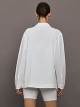 Model wears white collared linen jacket with buttons down the front and long sleeves.
