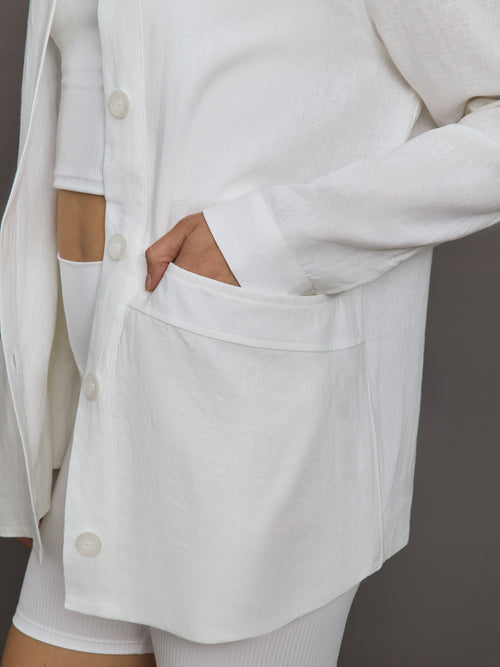 Model wears white collared linen jacket with buttons down the front and long sleeves.
