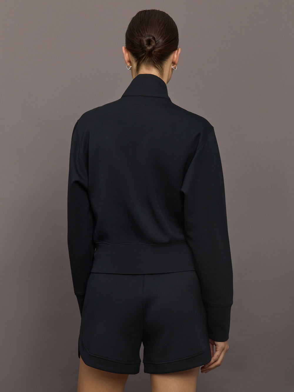 Model wears black Interlock Full Zip Jacket featuring a sleek, minimalist design with a high collar and full-length zipper.